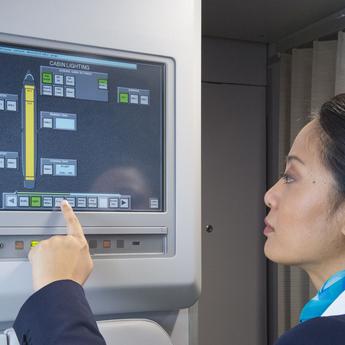 A flight attendant in uniform operating the Flight Attendant Panel (FAP) on the aircraft.