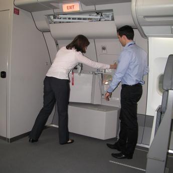 An instructor demonstrating and guiding a cabin crew trainee in closing the door of an aircraft during the training session.