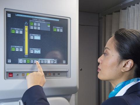 A flight attendant in uniform operating the Flight Attendant Panel (FAP) on the aircraft.