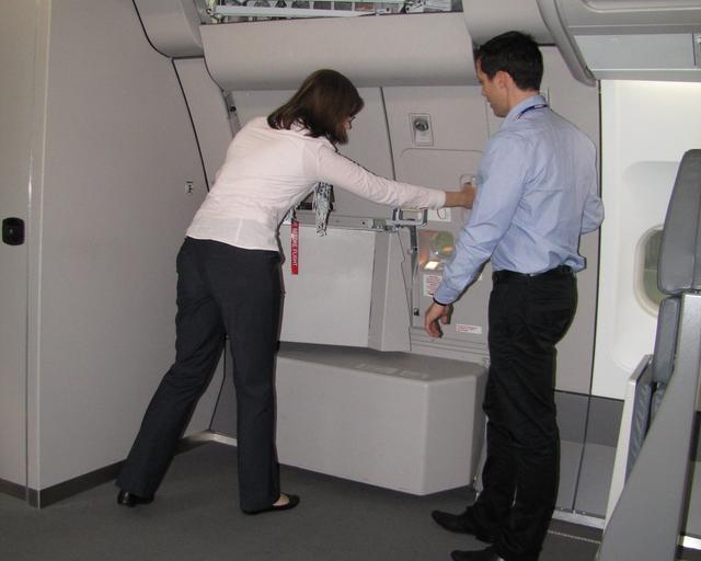 An instructor demonstrating and guiding a cabin crew trainee in closing the door of an aircraft during the training session. An instructor demonstrating and guiding a cabin crew trainee in closing the door of an aircraft during the training session.
