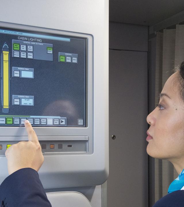 A flight attendant in uniform operating the Flight Attendant Panel (FAP) on the aircraft.