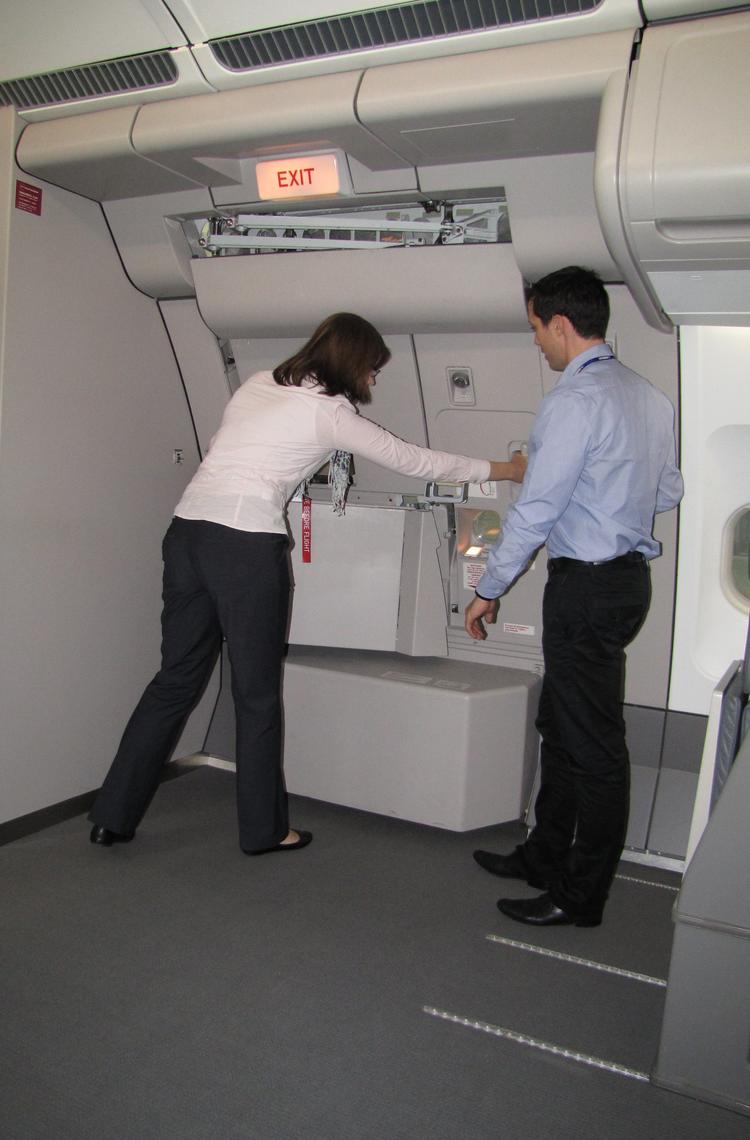 An instructor demonstrating and guiding a cabin crew trainee in closing the door of an aircraft during the training session.